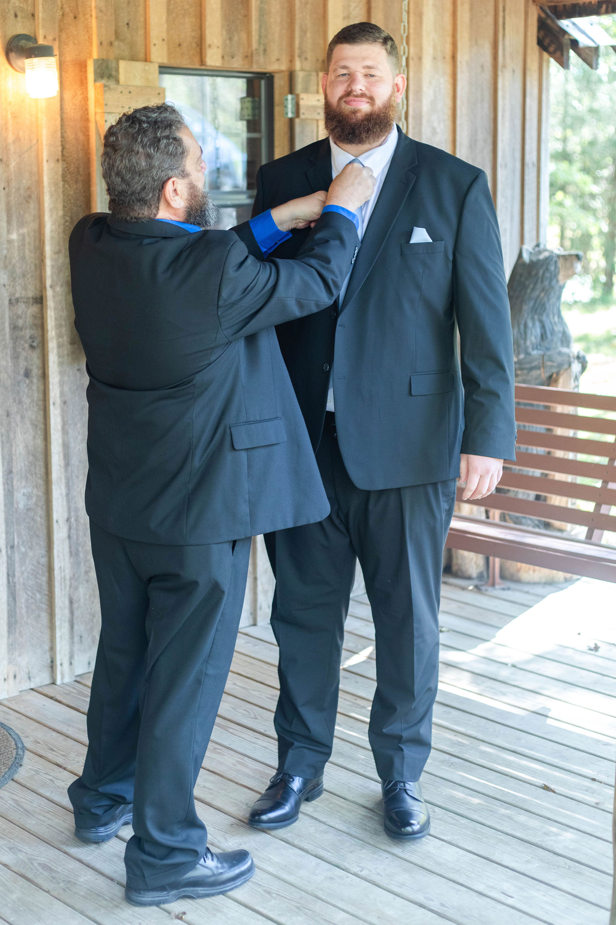 the groom's father fixes his tie on the porch of the Groom's Cabin at The Barn at Cedar Grove