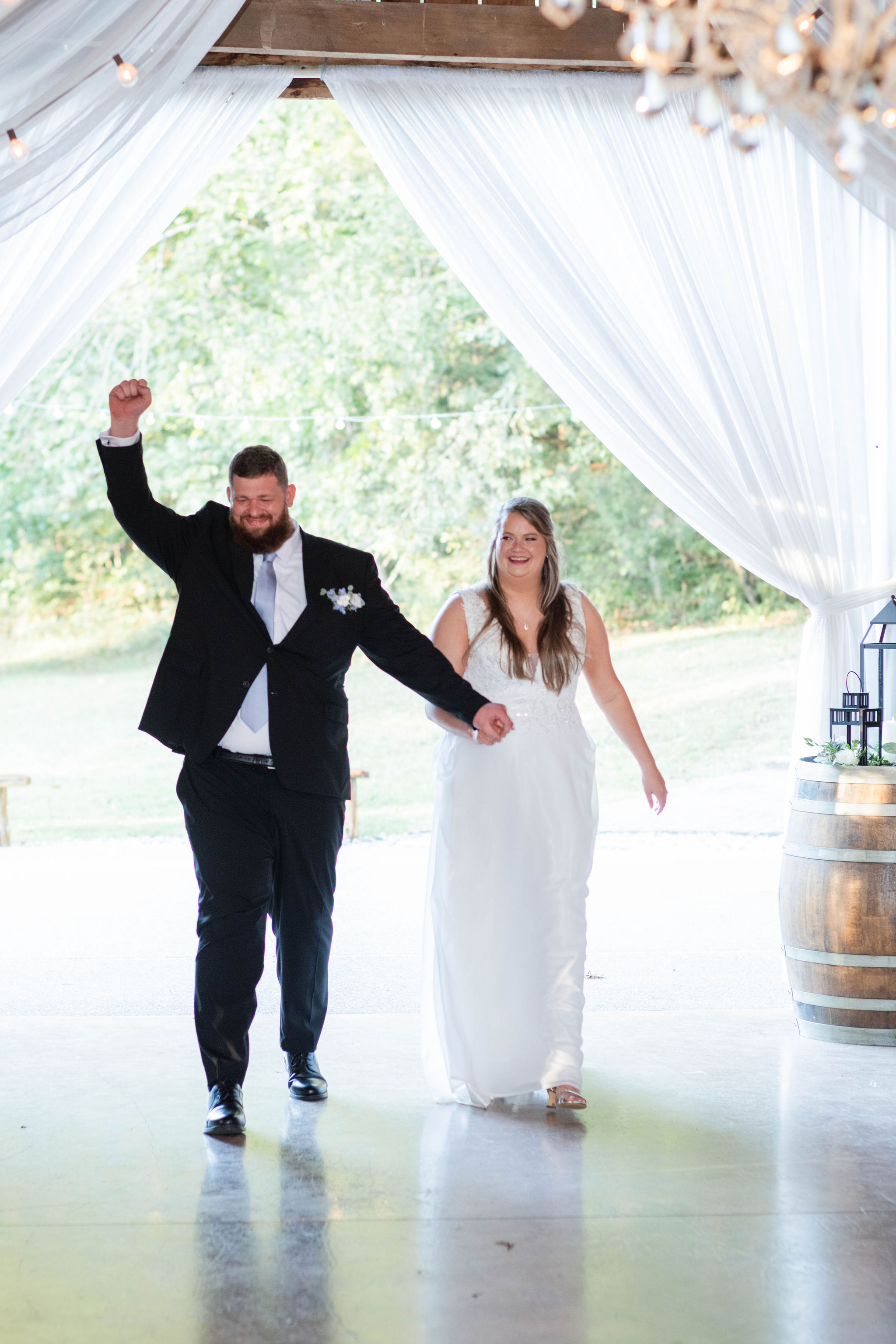 Groom raises his hand with excitement as he and his new bride enter the wedding reception at The Barn at Cedar Grove 