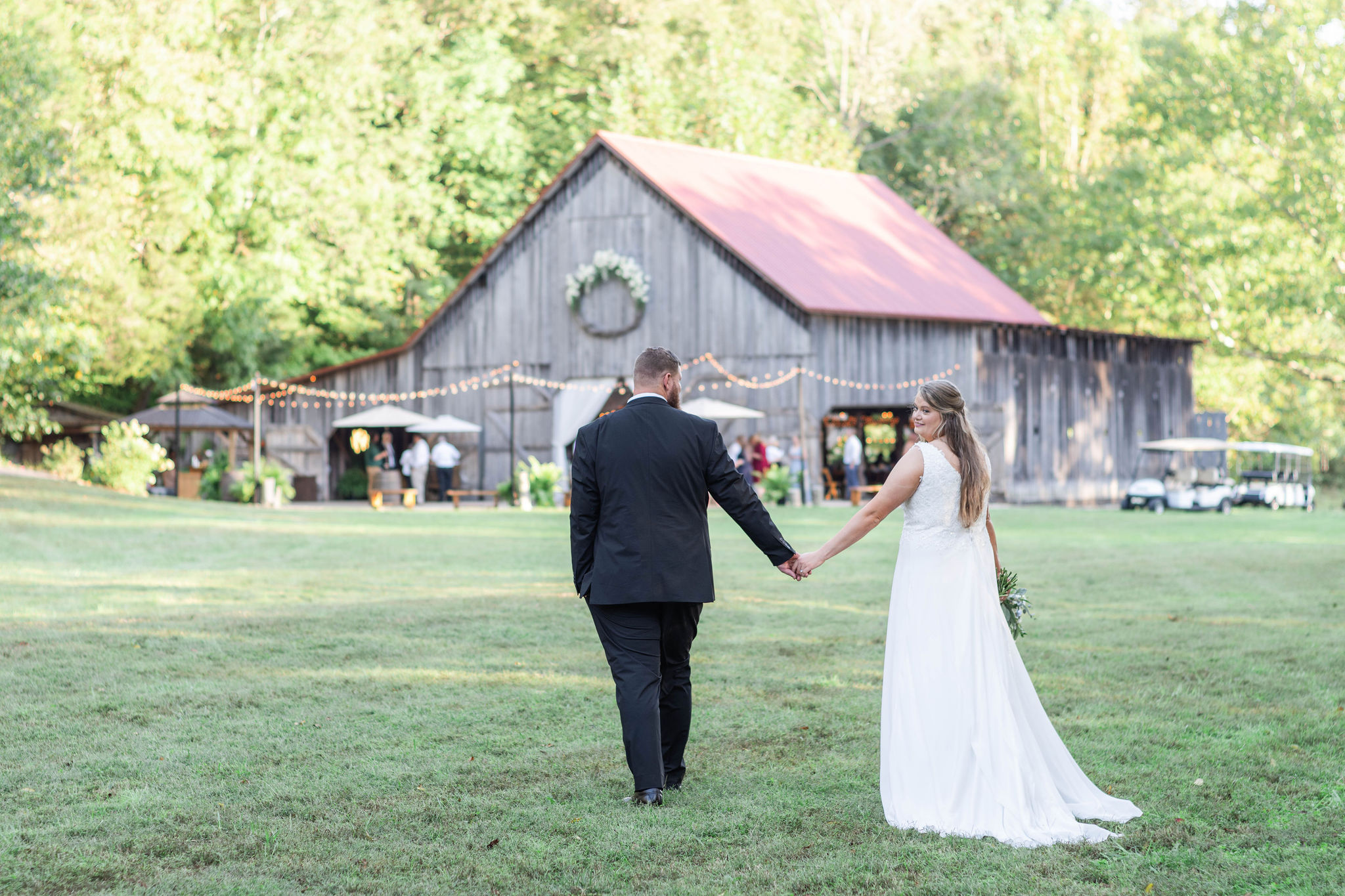 Hannah & Michael walk across the shaded meadow toward The Barn at Cedar Grove