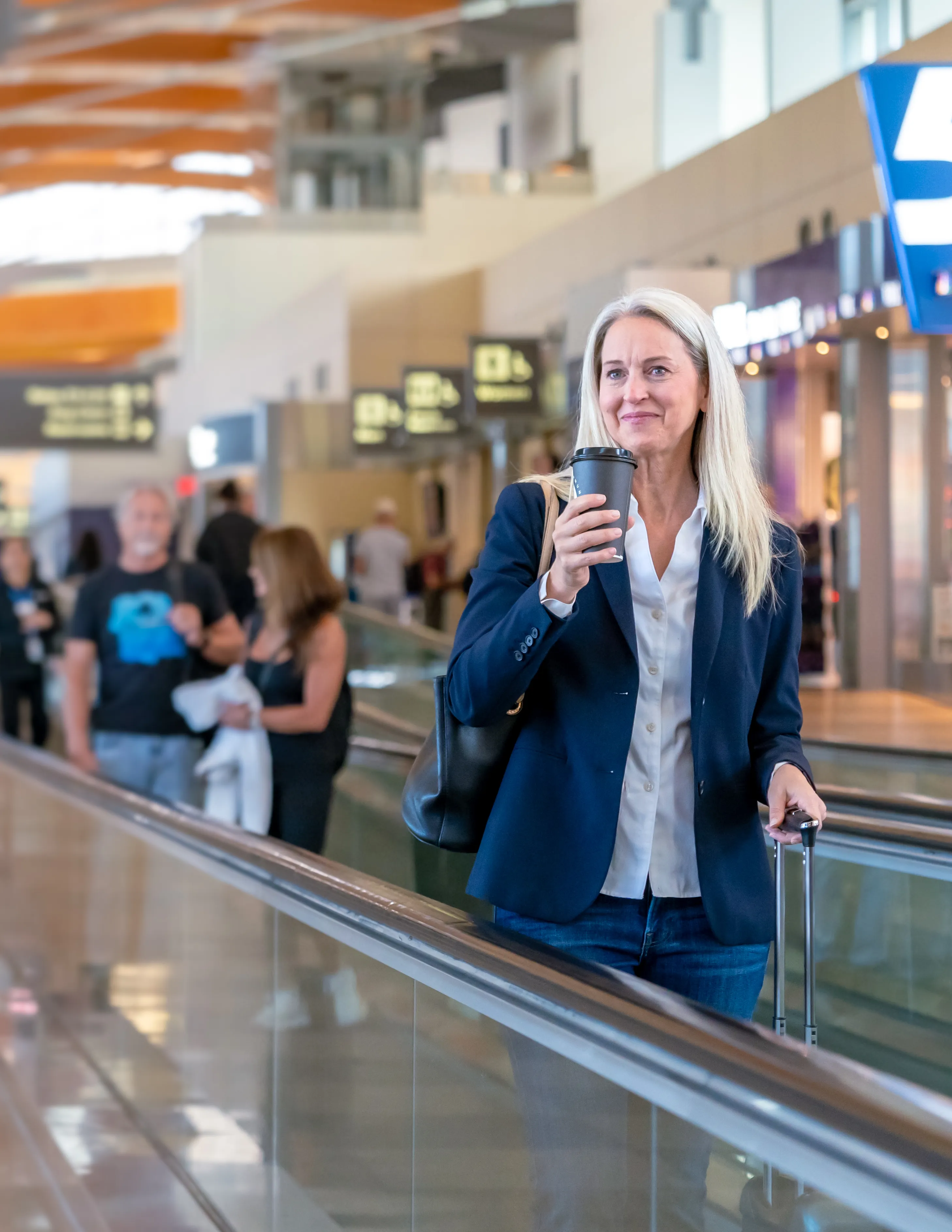 Woman in a blazer holding a coffee on a people mover inside Terminal 2 of Raleigh-Durham International Airport during a video shoot for the airport authority.