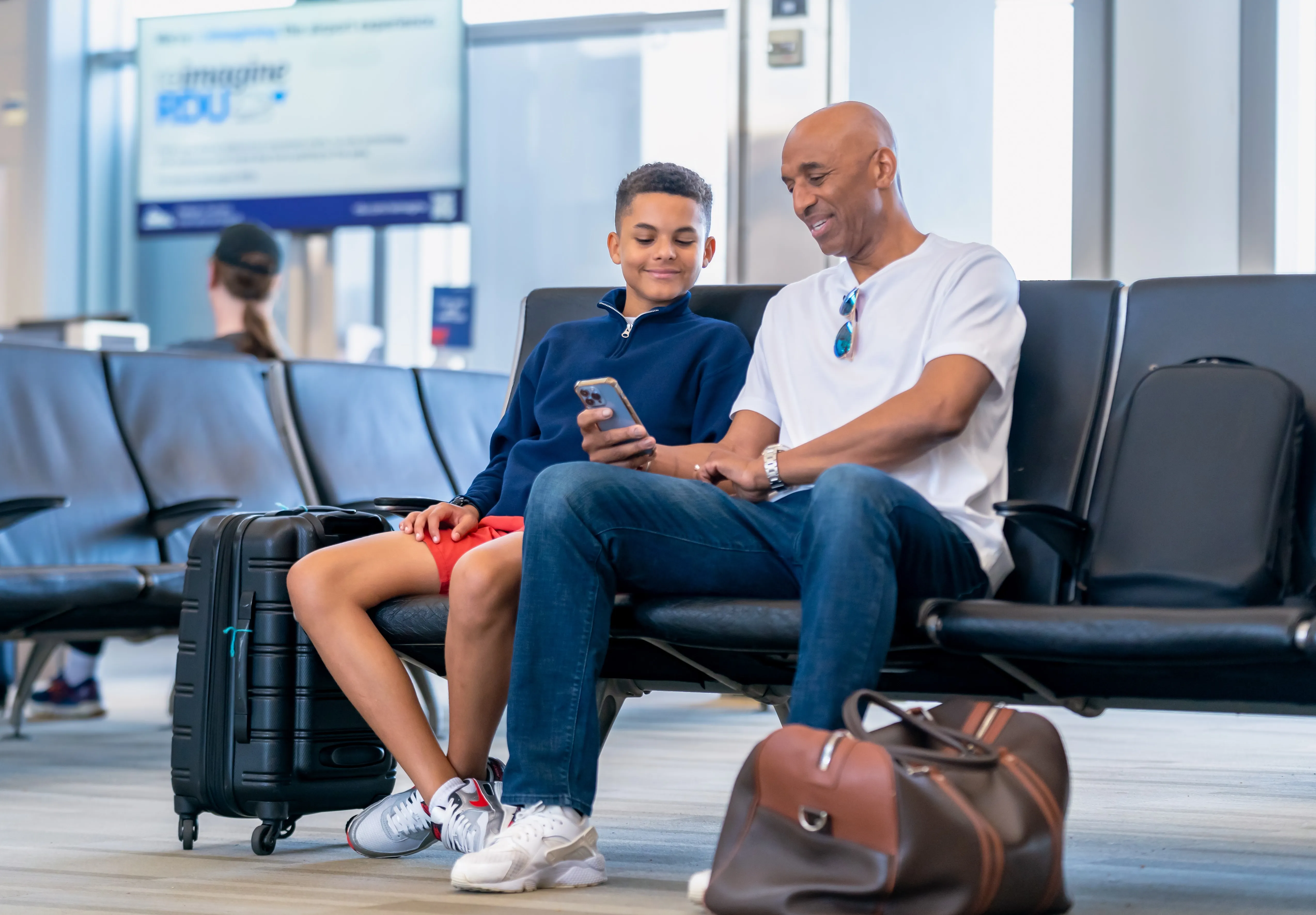 Father and son looking at a phone at their gate in Raleigh-Durham International airport for a video shoot with the airport authority.