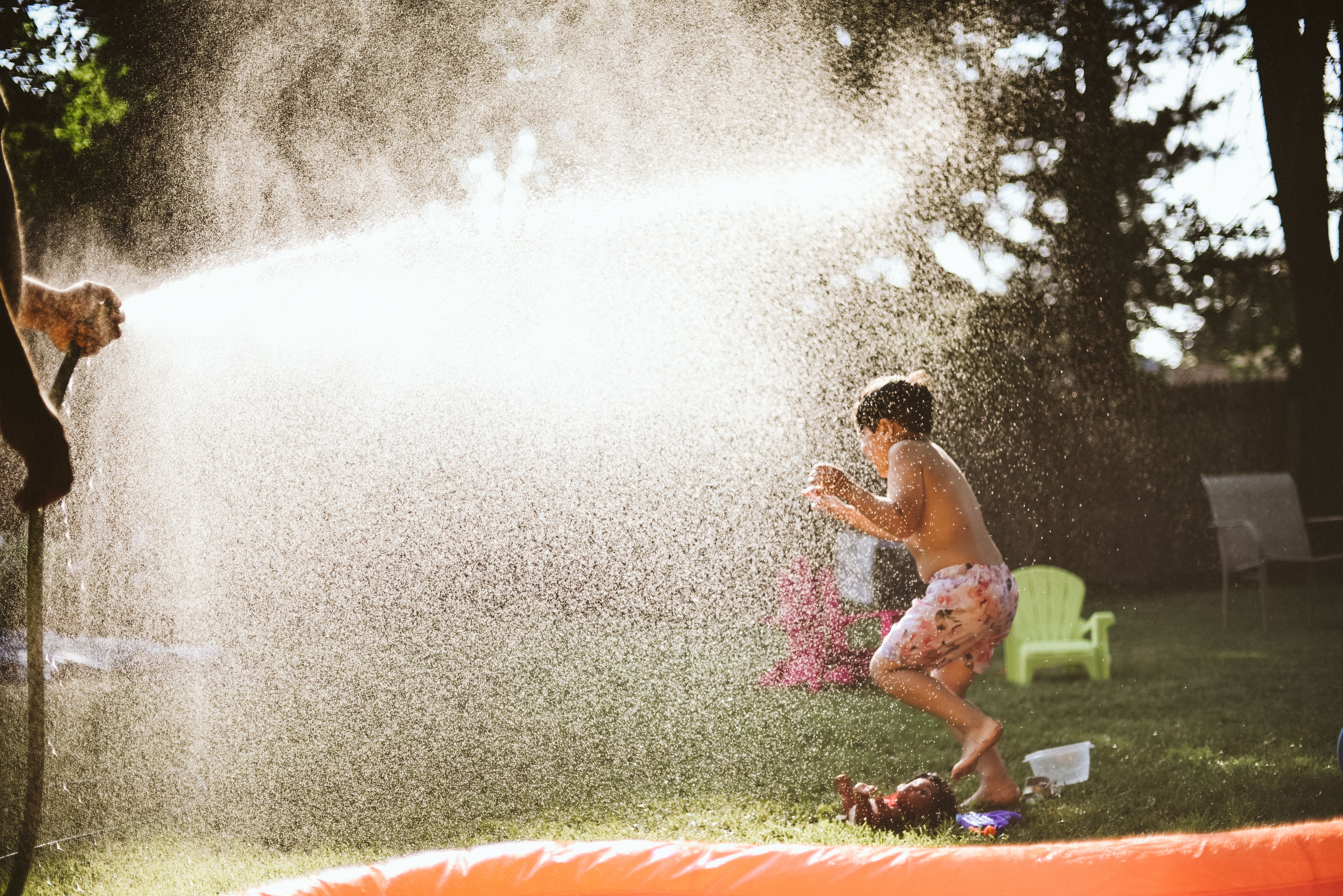 A child playing outdoors in a backyard sprinkler on a sunny summer day