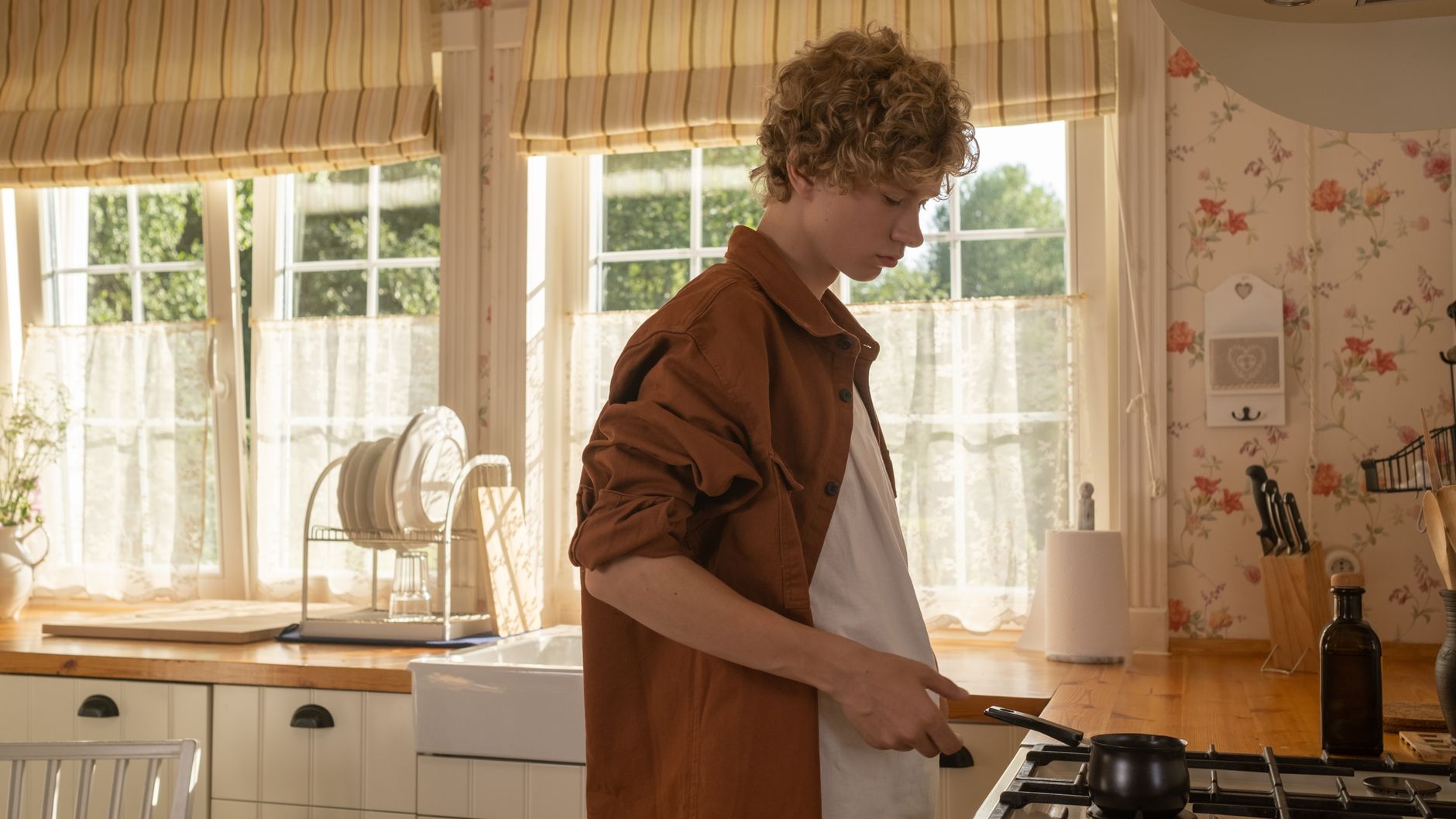 A teenager cooking at the stove in a sunlit home kitchen