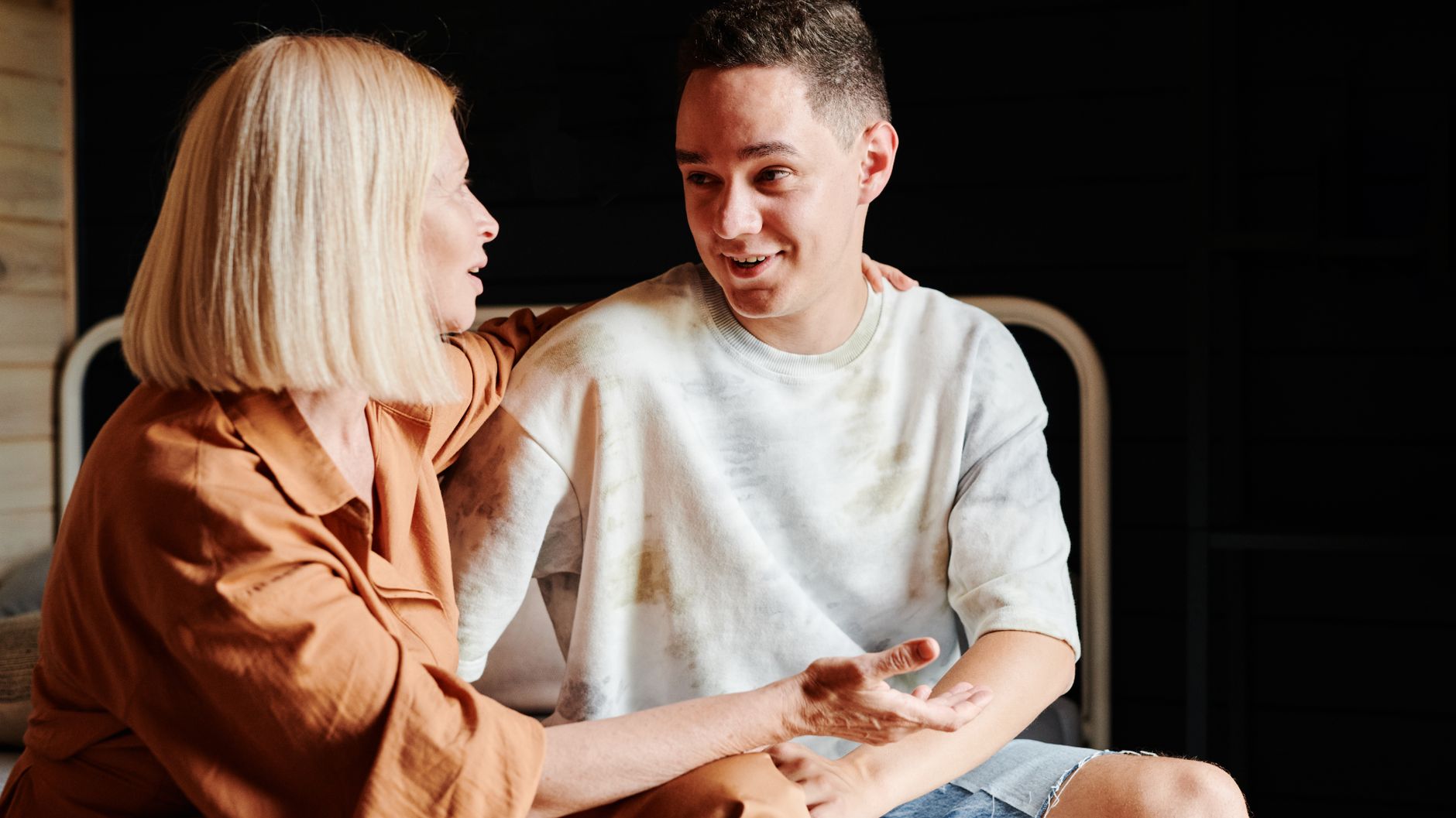 A parent and her adult son sitting side by side at home, in the middle of a conversation