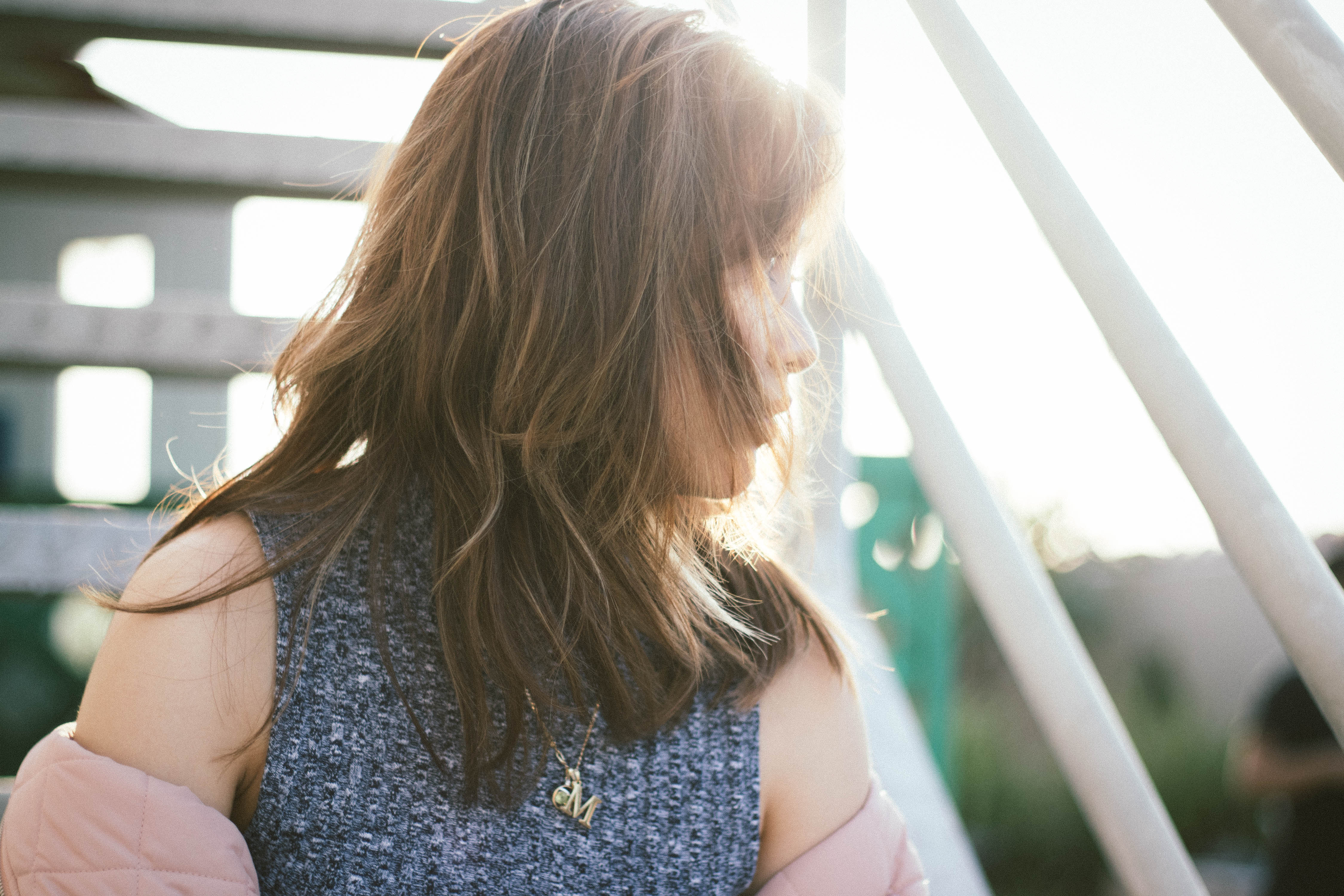 Photo of girl with brown hair and wearing a gray knit top looking to the right, against the light of the sun
