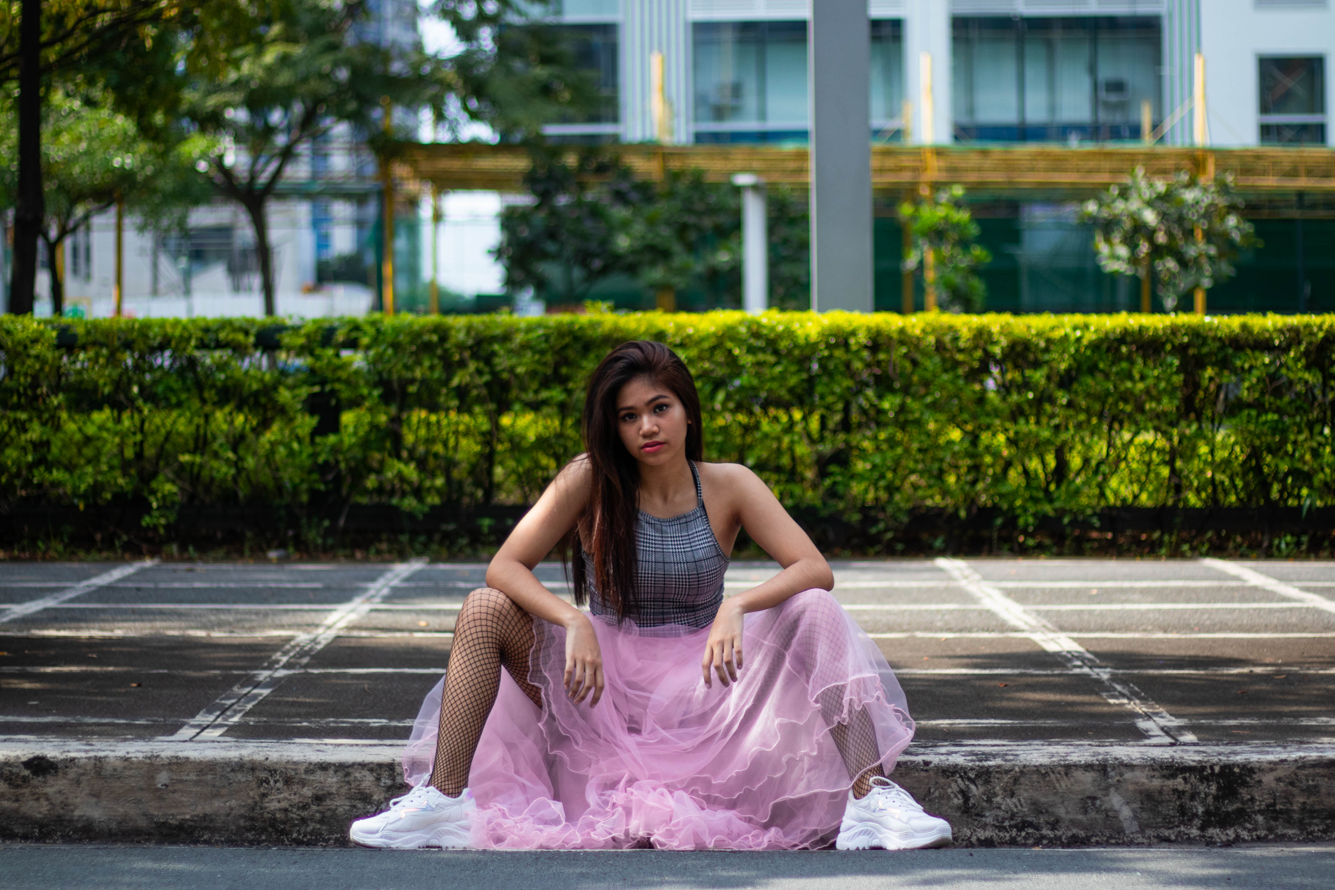 Girl in a pink tulle skirt and white sneakers sitting on the sidewalk