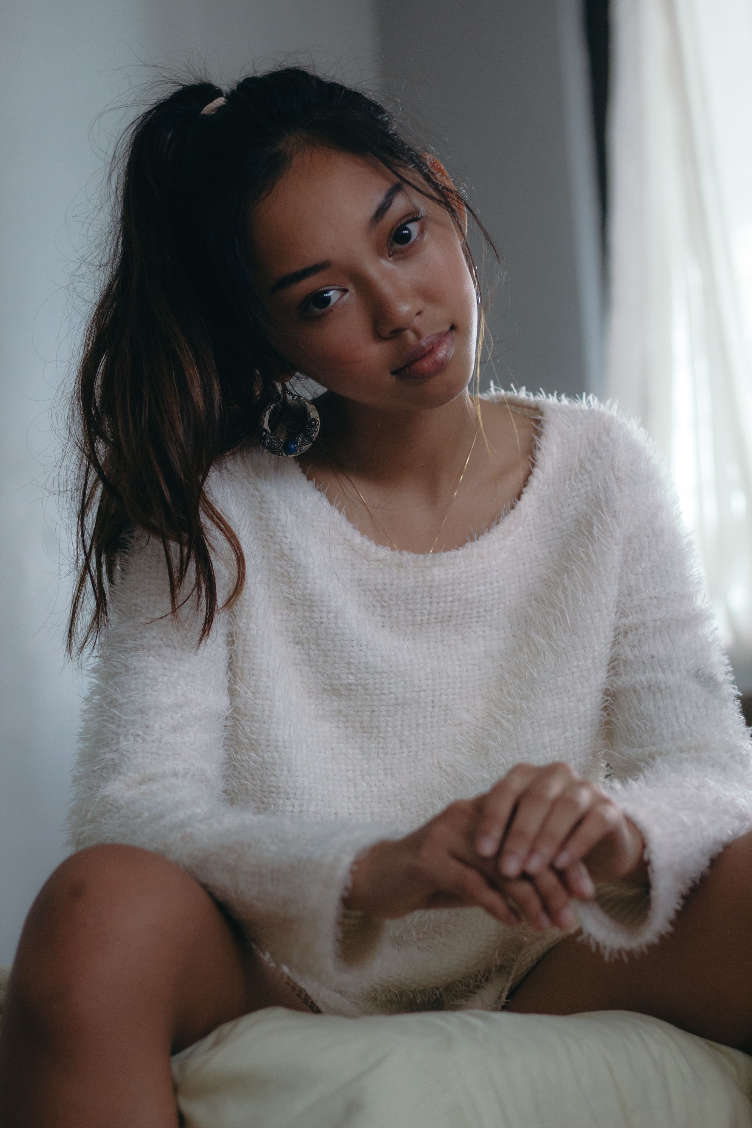 Portrait of a girl in white sweater sitting on the edge of the bed