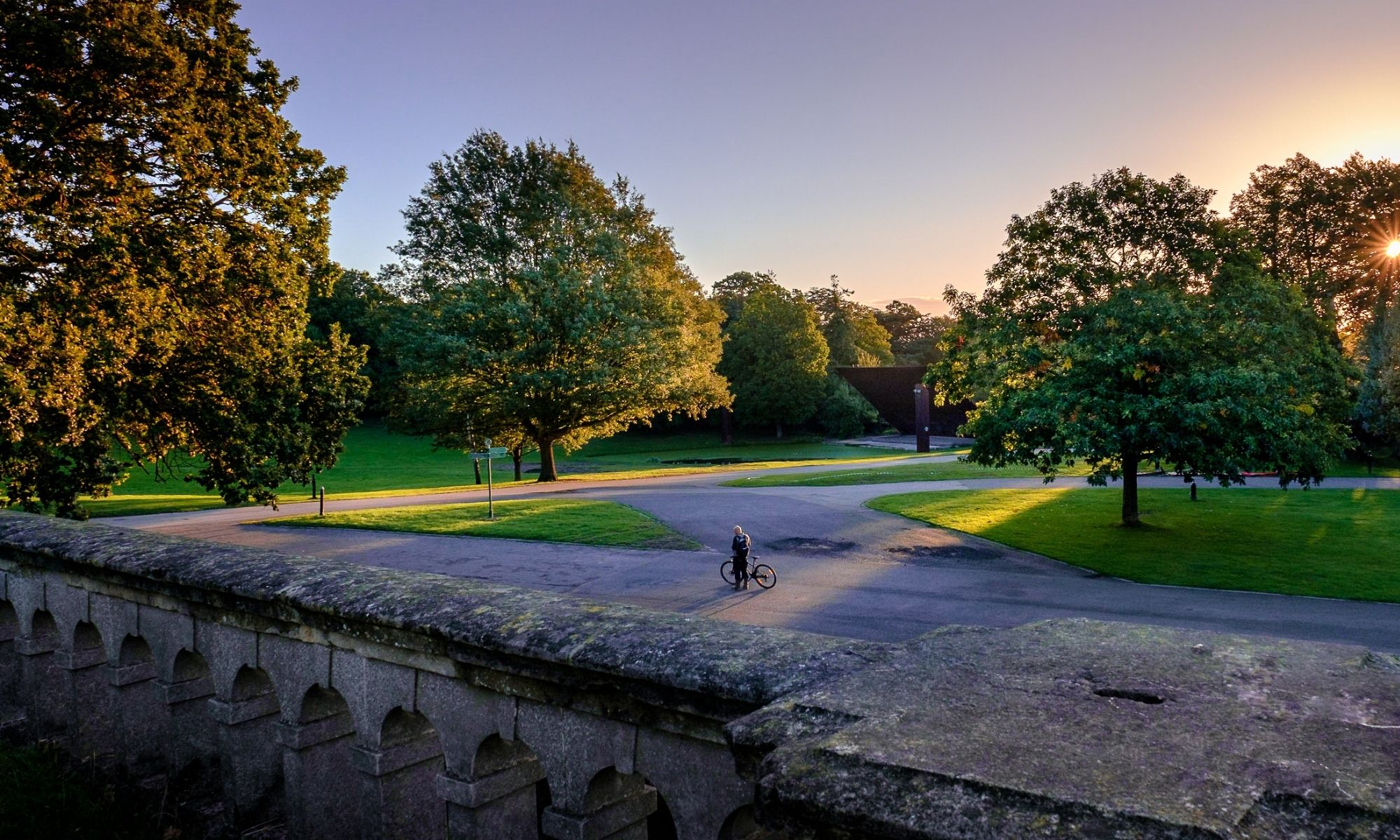 View of green trees and one person standing near a bicycle
