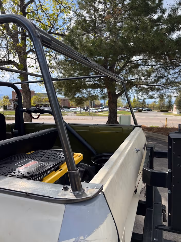 Close-up of an open white truck bed with a black roll cage and some cargo mats inside, parked near trees and a parking lot.