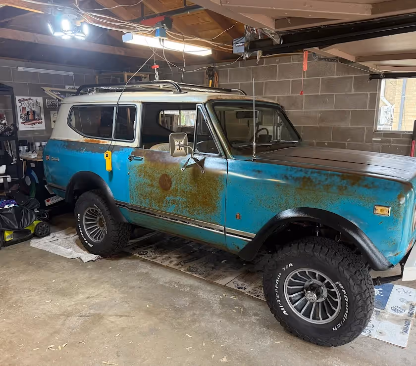 Rusty blue and white vintage International Scout II SUV parked inside a garage with off-road tires and roof rack.
