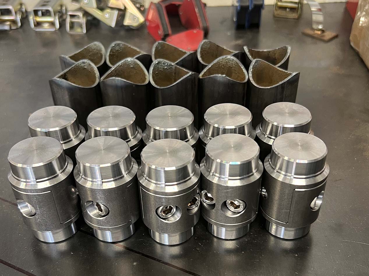 Six metal pipe beveling or cutting tool heads lined up on a perforated metal workbench with additional tools and hooks in the background.