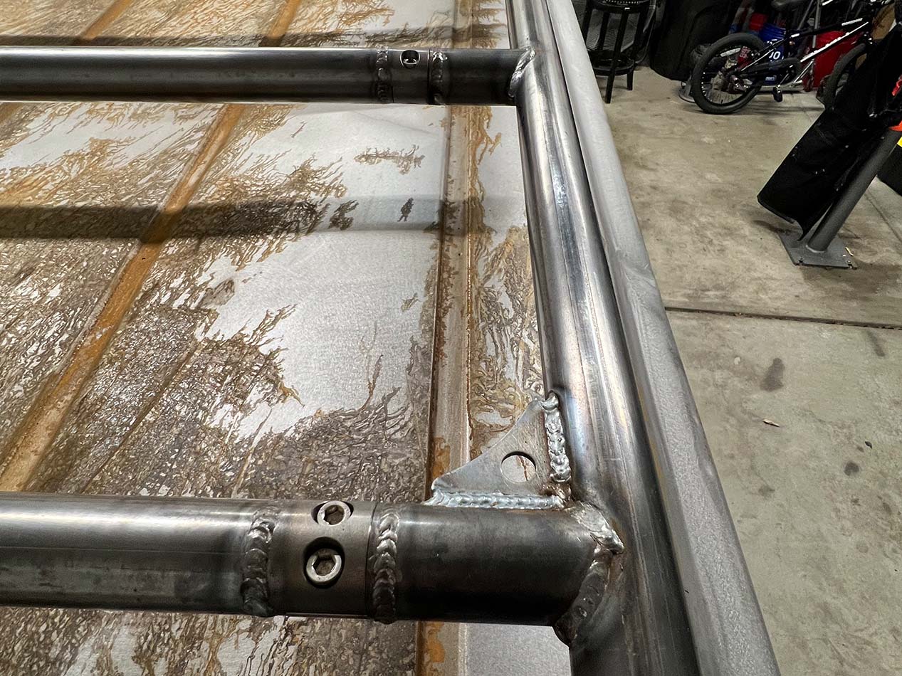 Close-up of welded stainless steel tubes with a clamp and joint on a workshop table.