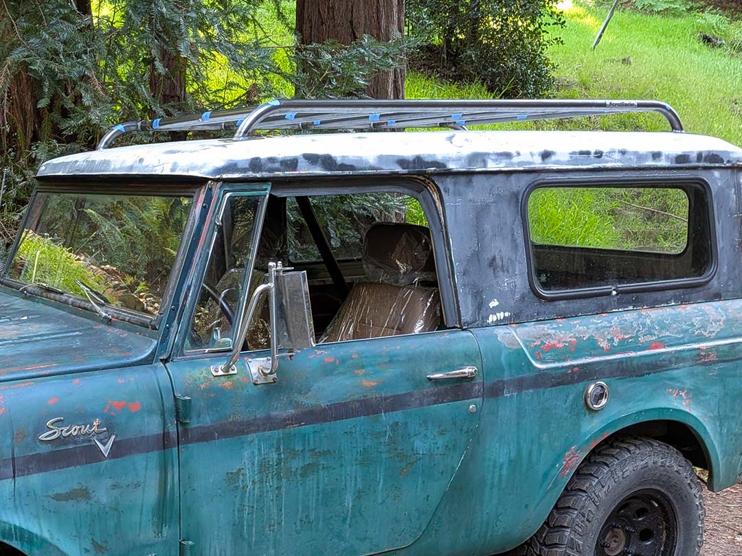 Close-up of a white Scout II roof with a Scout Racks roof racks, parked outdoors with trees and houses in the background at sunset.