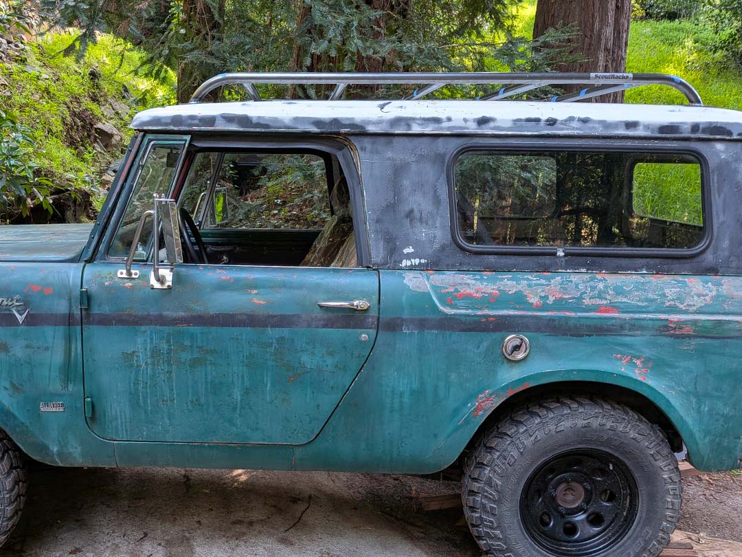 White Scout II with a bare metal Scout Racks roof rack, and rear-mounted tire carrier in a parking lot.