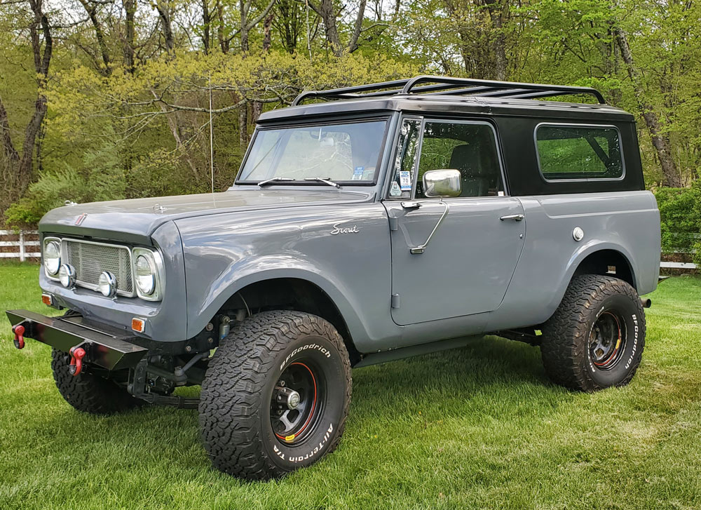 Rusty blue and white vintage International Scout II SUV parked inside a garage with off-road tires and roof rack.