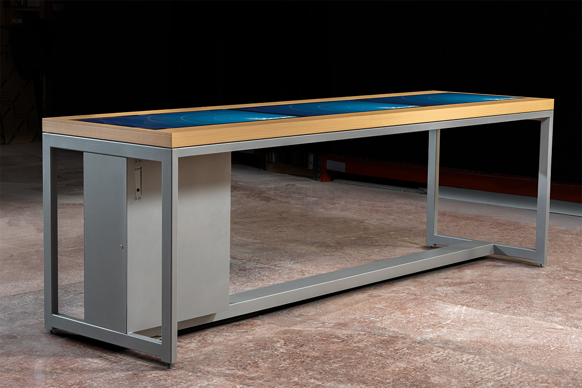 This wood and metal touch table features a triple 43” display setup, with the top and base designed to match the client’s existing, non-touch furniture. 