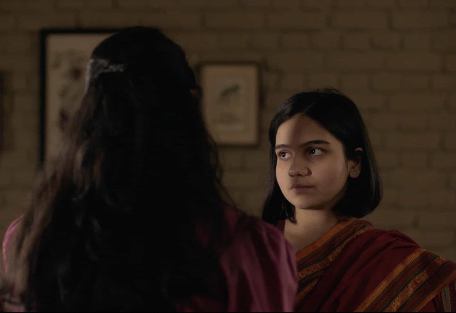 Movie still from Girls Will Be Girls. A young woman looks at another woman, that woman's back to the camera.