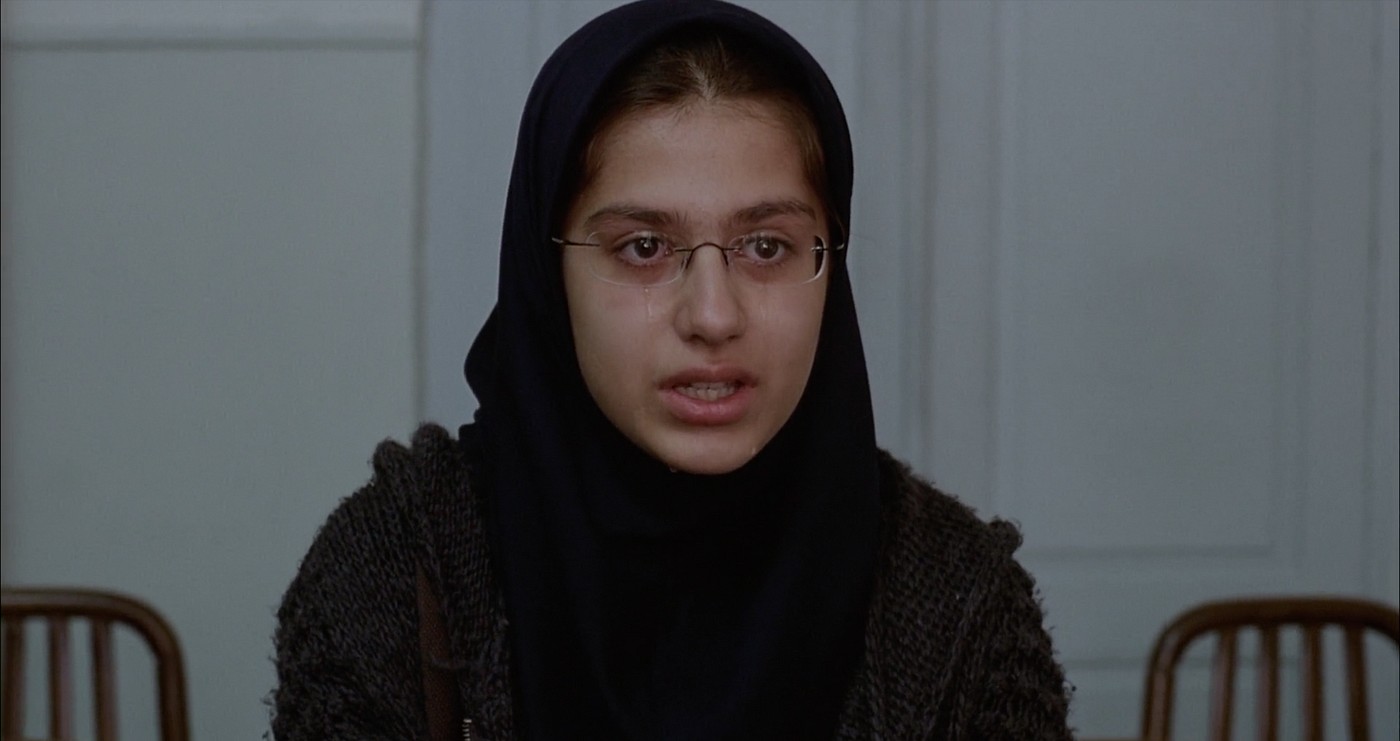 Movie still from A Separation. A young girl with a hijab and glasses sits with tears streaming down her face.