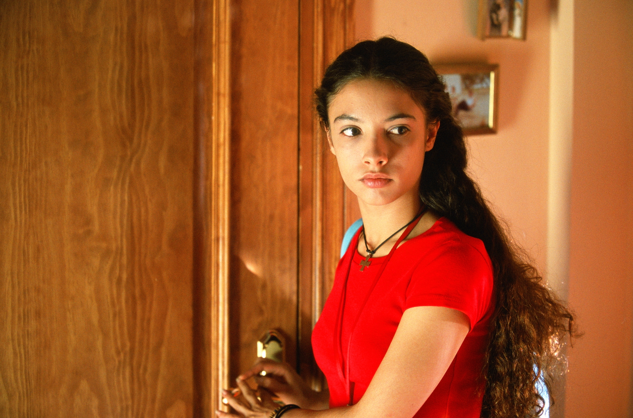 Movie still from Volver. A young girl stands in front of a door inside, looking solemn.
