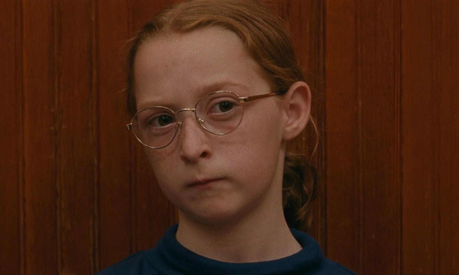 Movie still from Janet Planet. A young girl with glasses looks offscreen, stern and pensive.