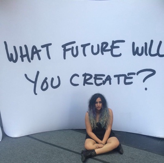 Namah as a teen sitting in front of a wall that says in big text "What future will you create?"