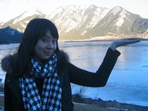 Steph as a teen holding her hand up to a beautiful skyline of mountains in front of a lake.
