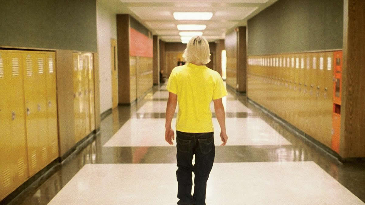 Movie still from Elephant. A teen boy walks down an empty hall.