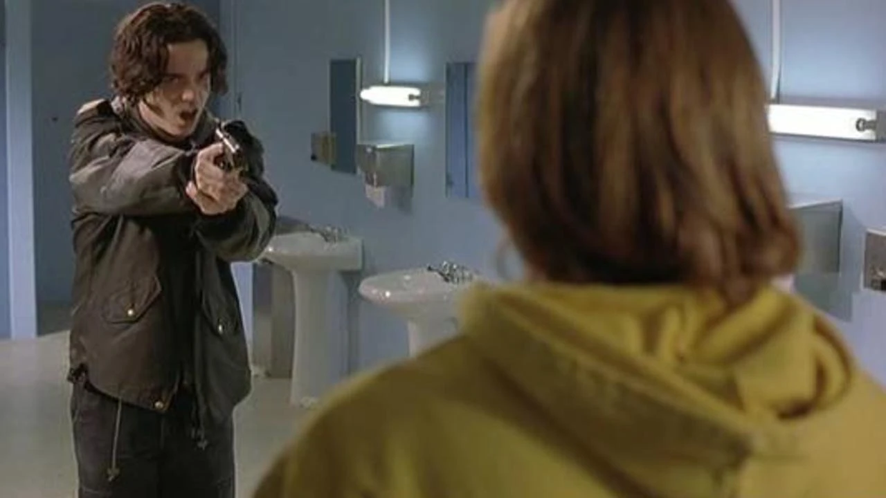 Movie still from Heart of America. A teen boy holds up a gun in a high school bathroom to someone.