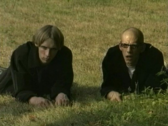 Movie still from Duck! Two teenagers lie down on a lawn, wearing all black.