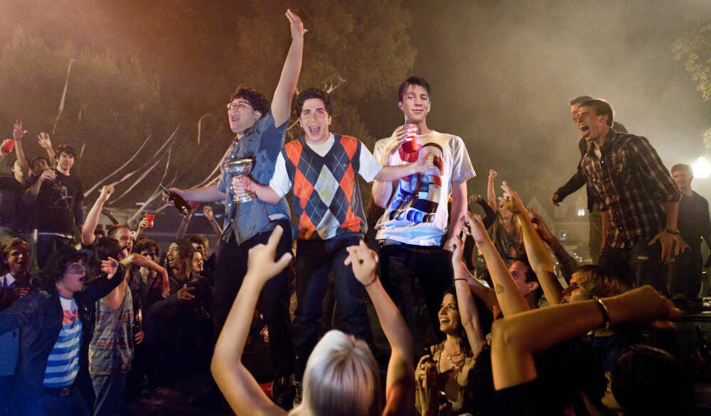 Movie still from Project X. Teen boys stand high above a huge group of partiers in a backyard.