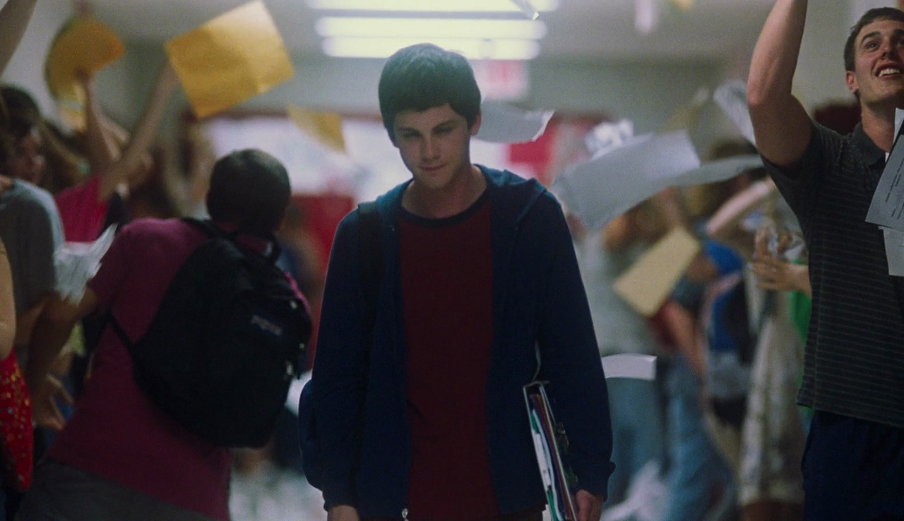 Movie still from Perks of Being a Wallflower. A teen boy walks down a hallway with people throwing papers in the air.