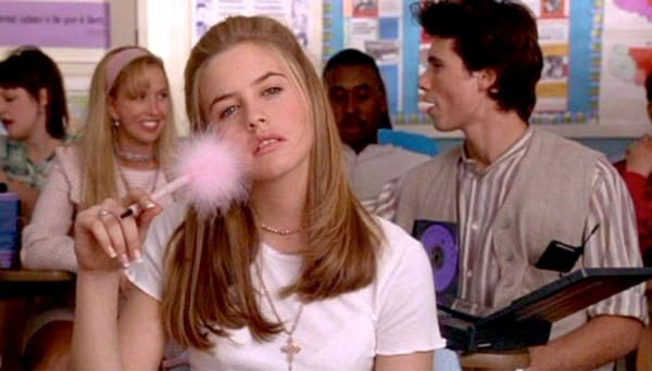 Movie still from Clueless. A teen girl sits in a classroom with a fluffy pink pen.