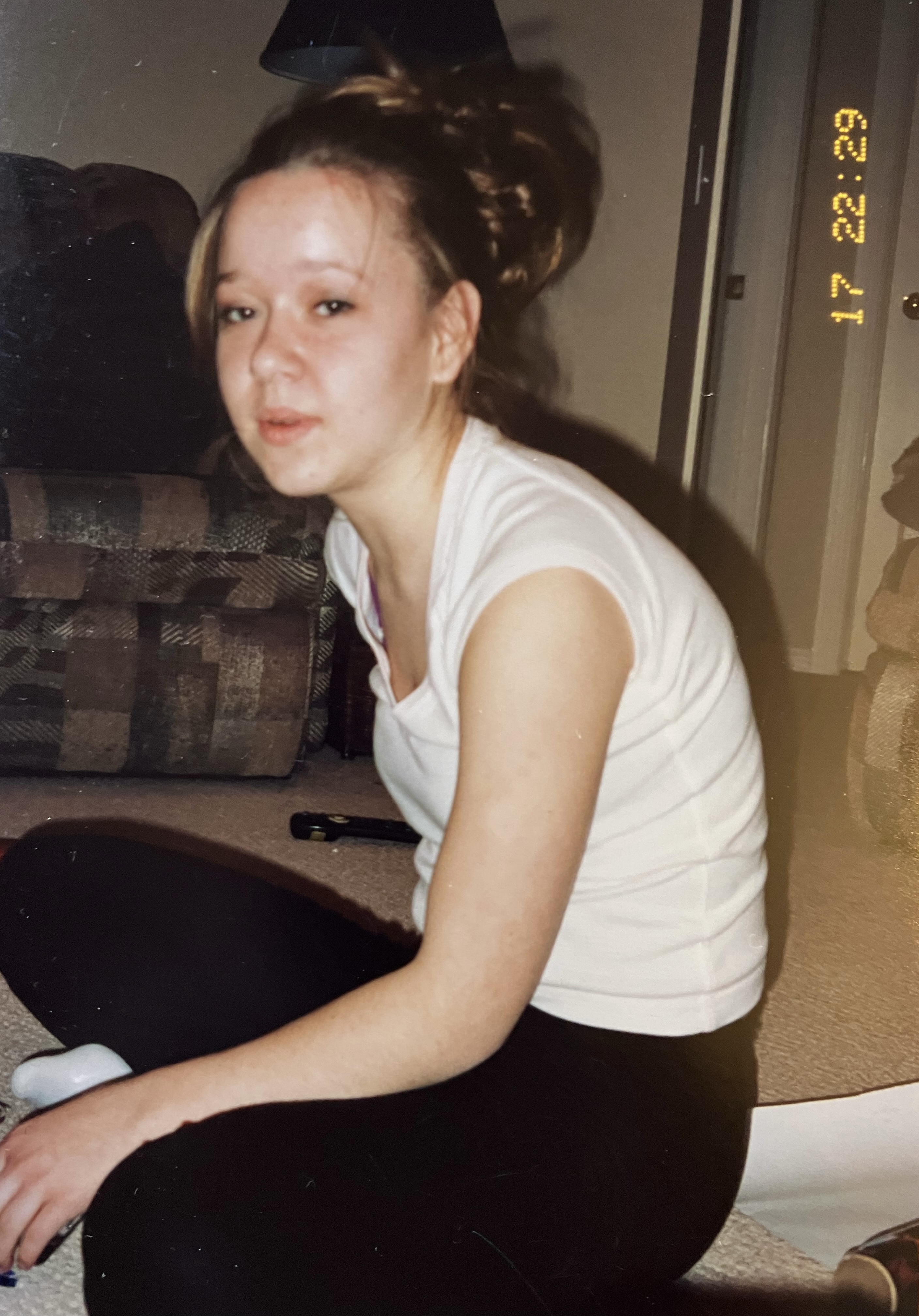 Beth as a teen sitting on the ground in a living room.