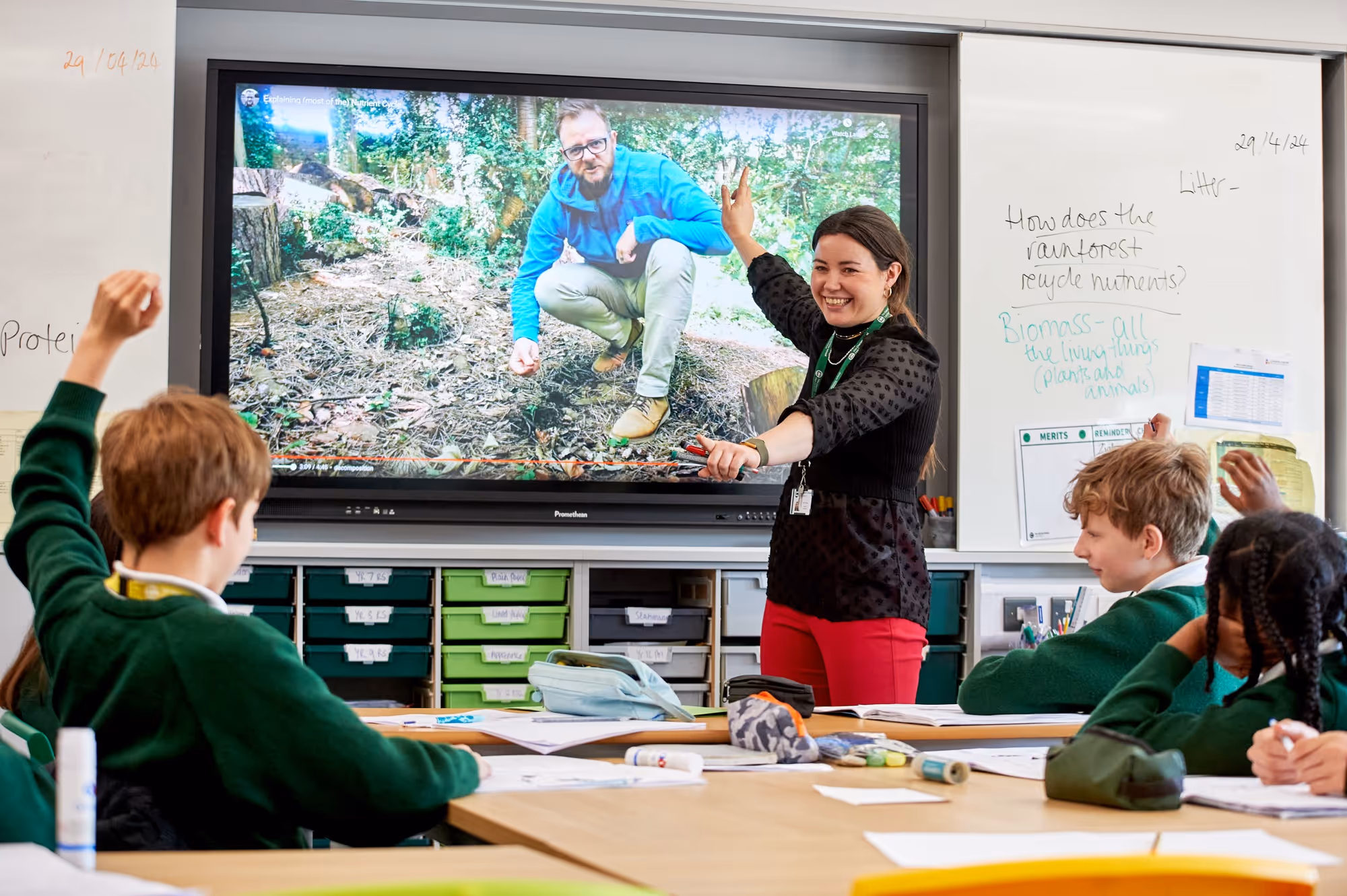A teacher standing at the white board pointing forward during a lesson