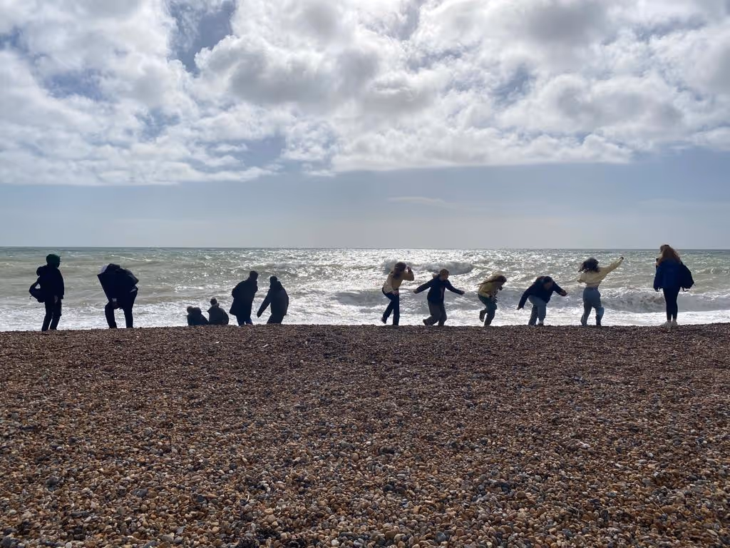 A group of students standing on a pebble beach looking out to sea