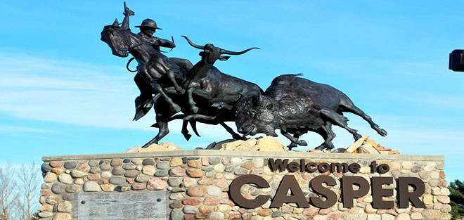 Bronze statue of a cowboy on horseback chasing a bull atop a stone platform with large letters reading 'Welcome to CASPER'.
