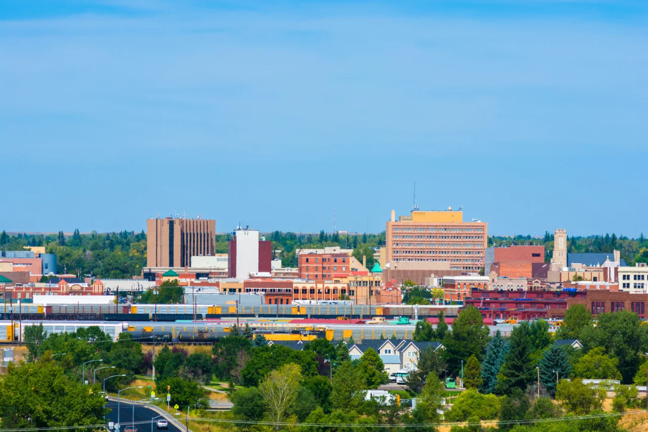 Downtown cityscape with mid-rise buildings, train cars, green trees, and clear blue sky.