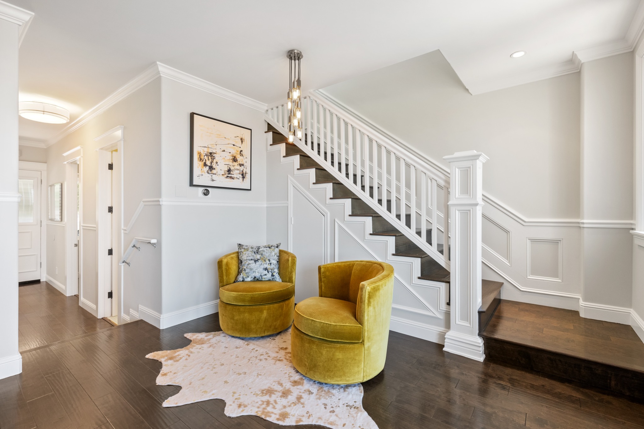 Bright entryway with a white staircase, wood floors and two gold accent chairs