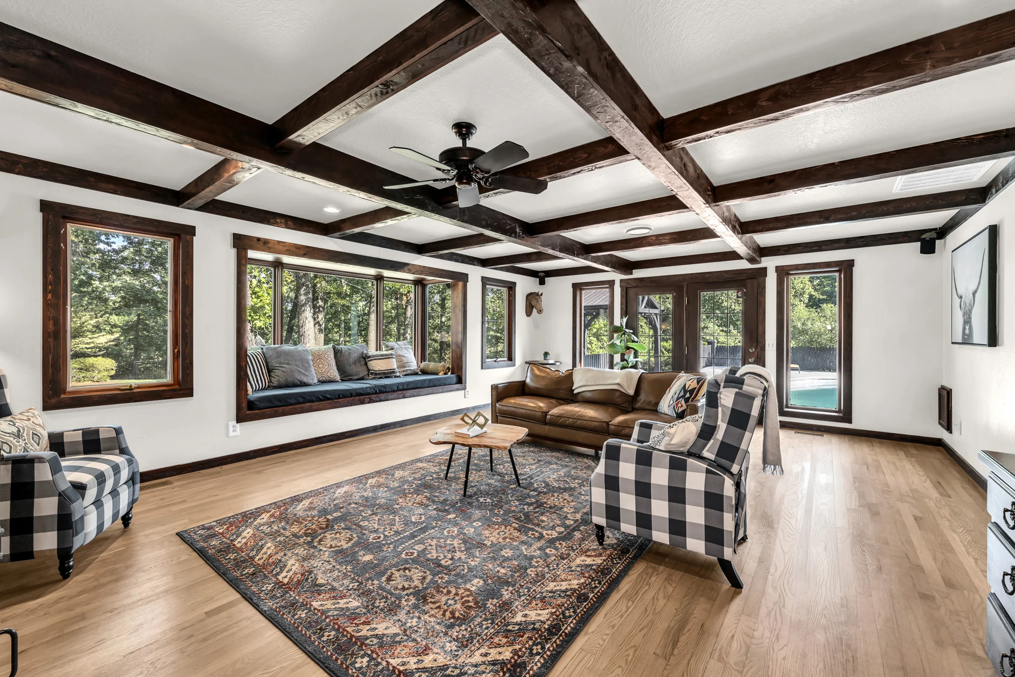 Living room with exposed ceiling beams, large windows and comfortable seating.