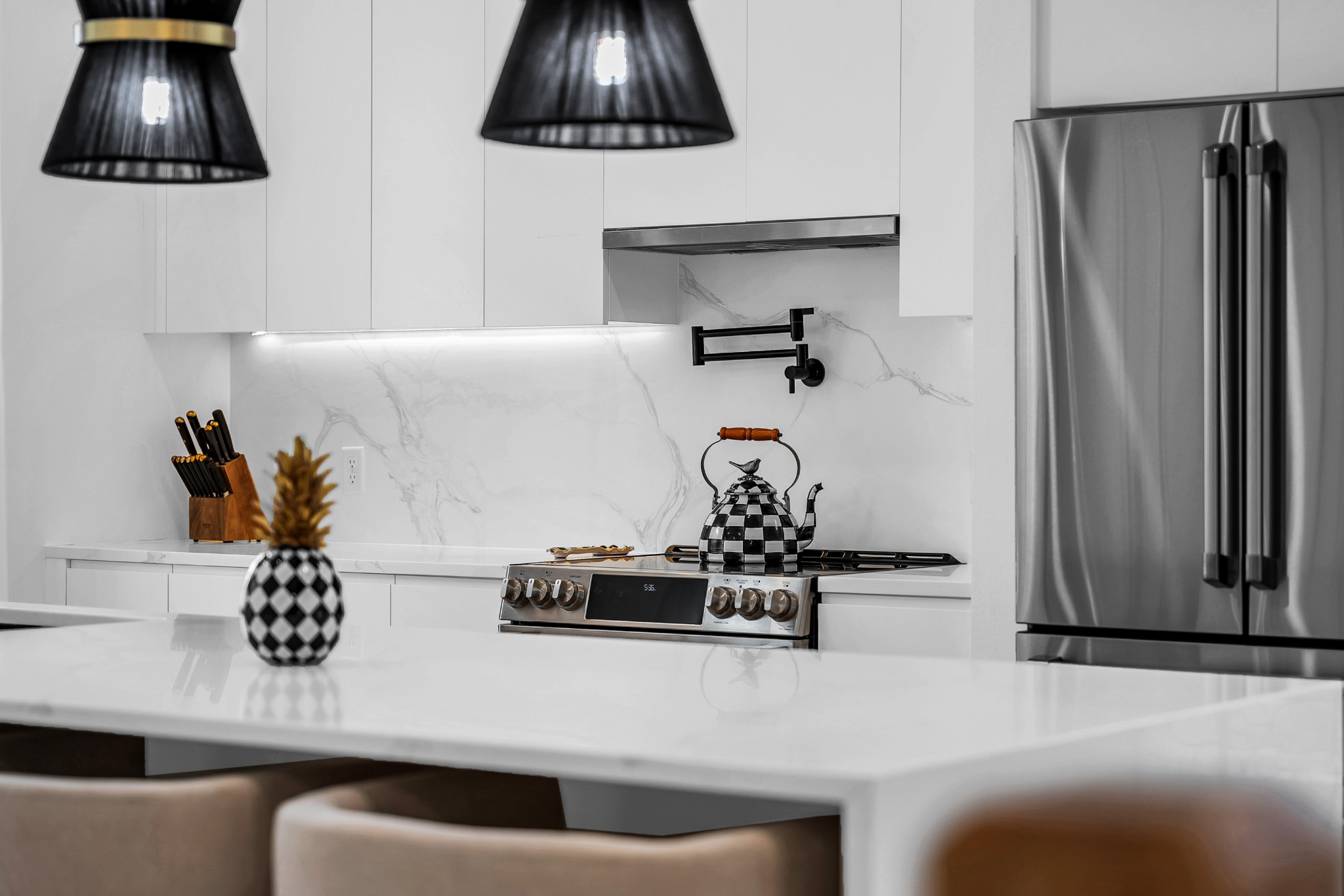 Modern white kitchen with black pendant lights, marble backsplash and stainless steel appliances.