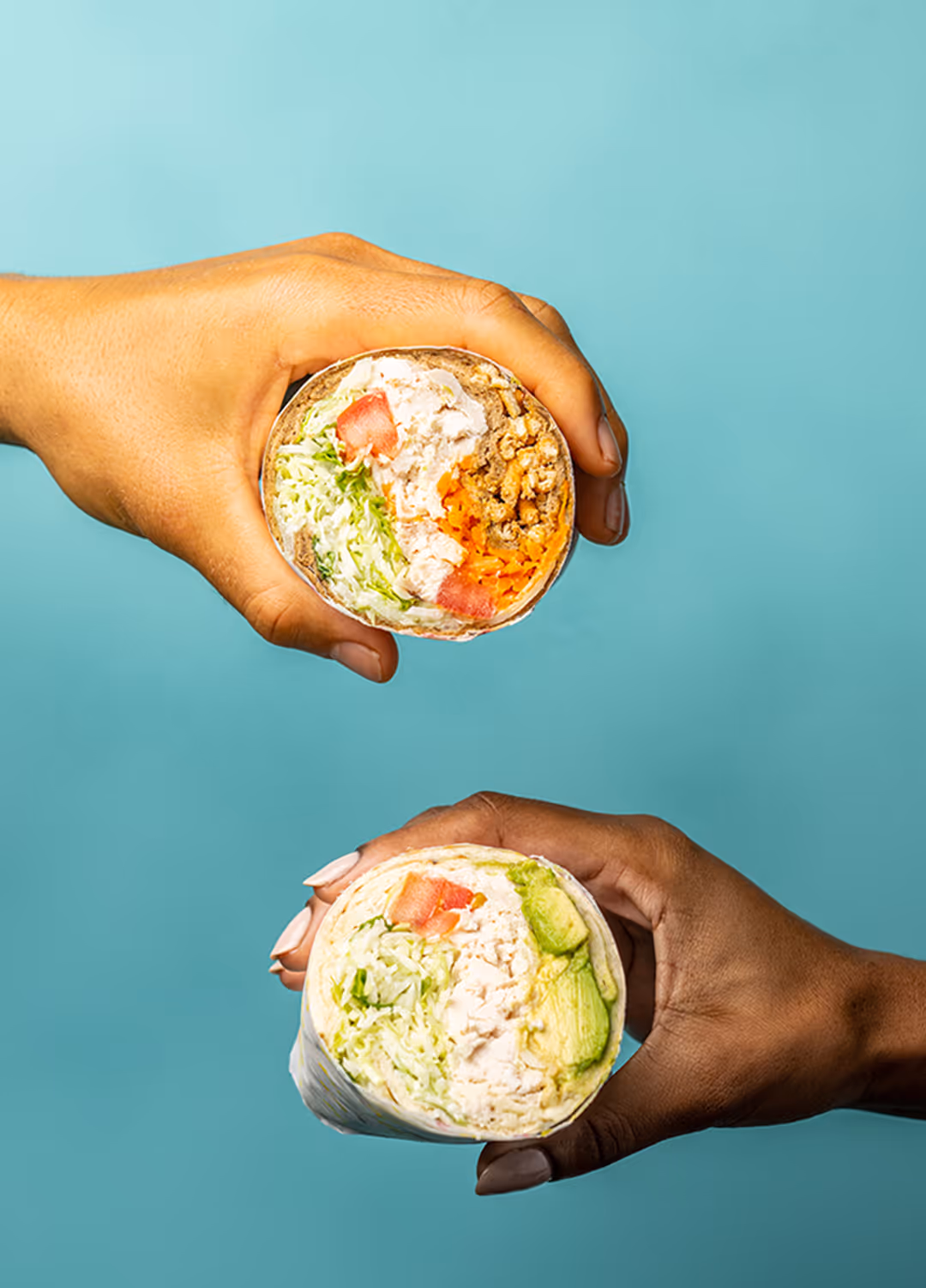 Hands holding chicken wraps.