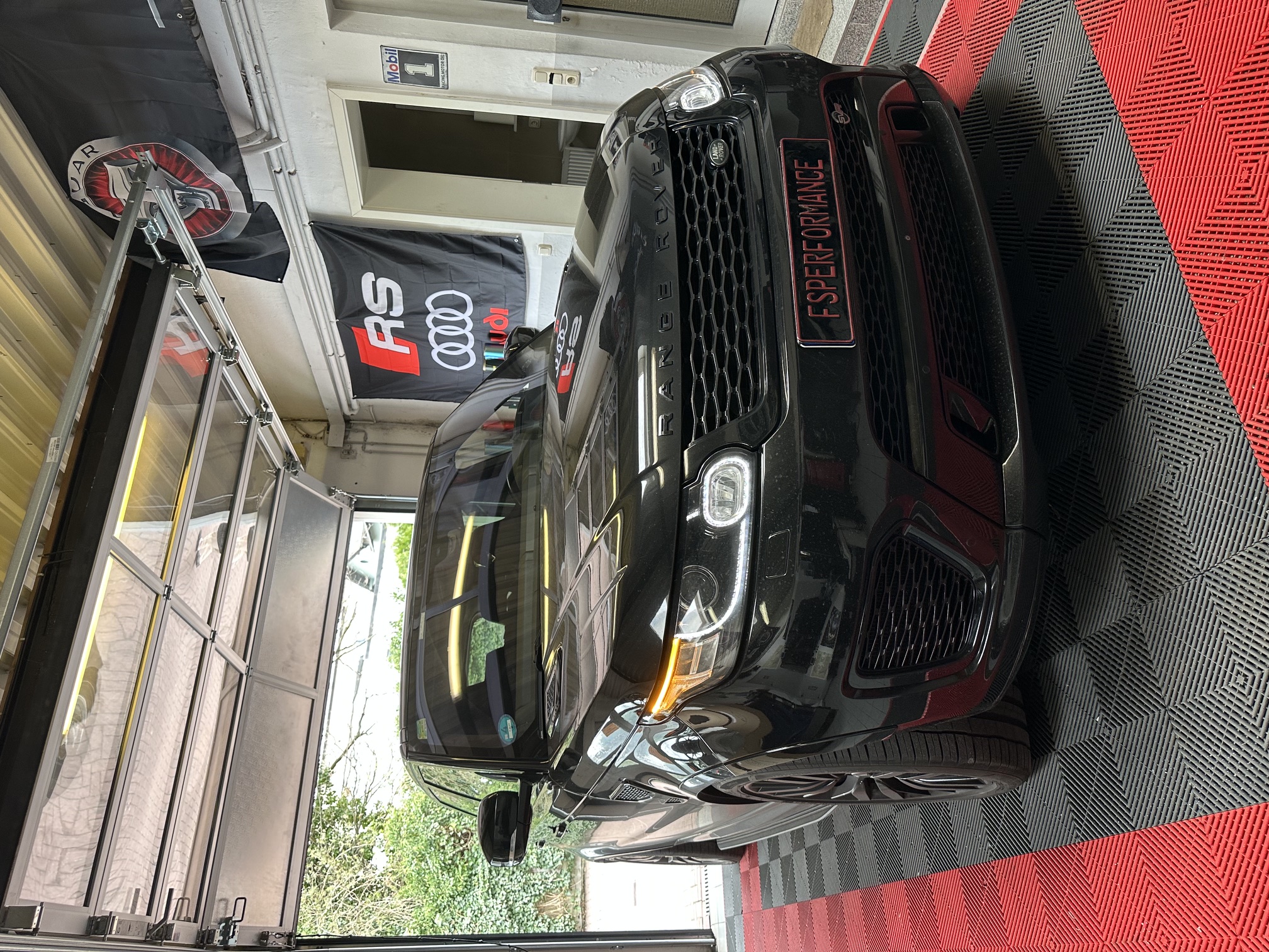 Frontansicht des schwarzen Range Rover Sport SVR mit Tagfahrlicht in der FS Performance Werkstatt mit Audi RS Banner im Hintergrund