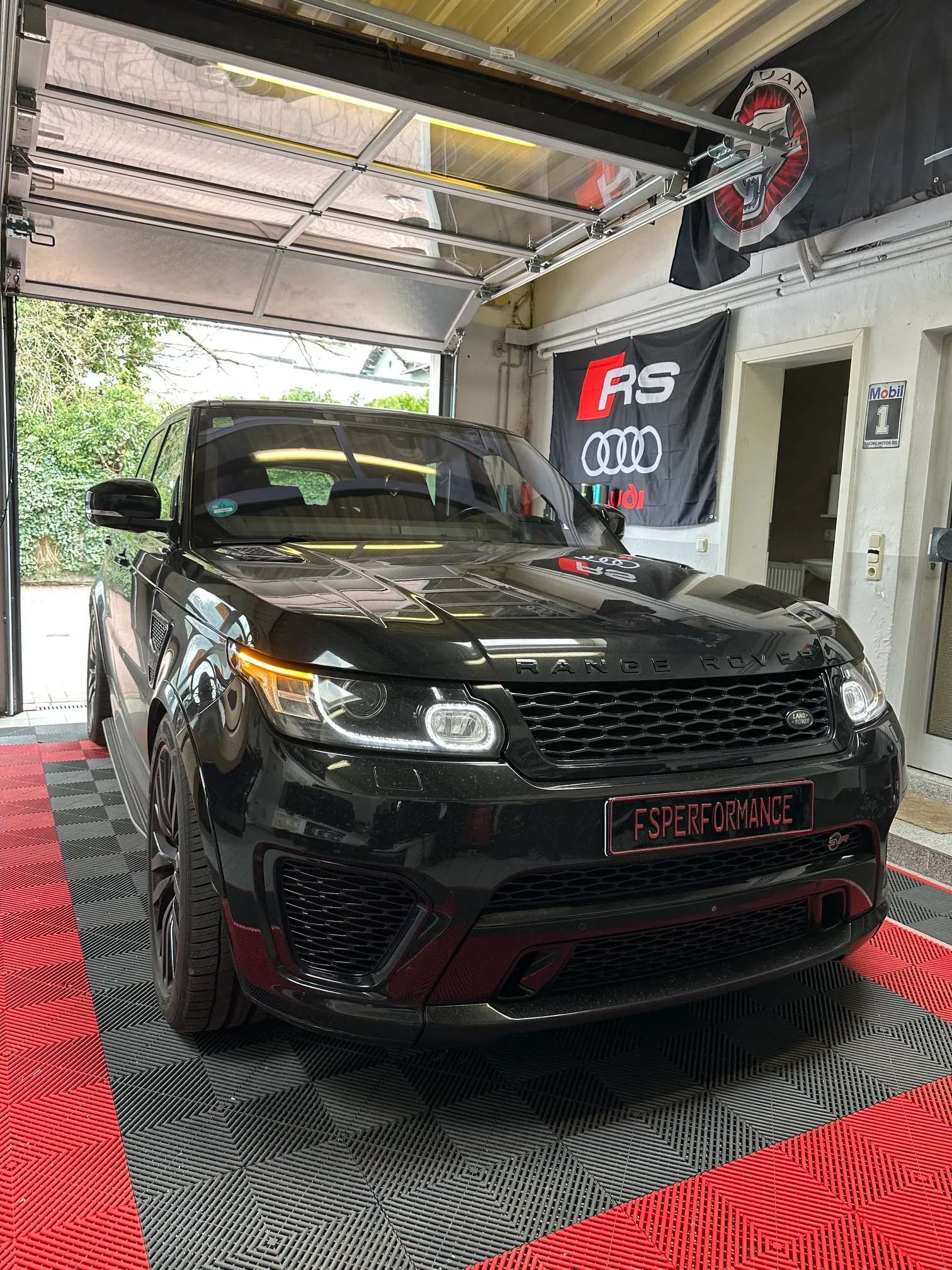 Frontansicht des schwarzen Range Rover Sport SVR mit Tagfahrlicht bei FS Performance mit Audi RS Banner im Hintergrund