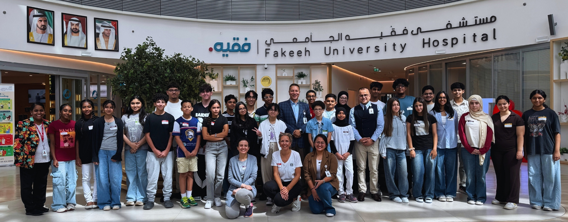Group photo of Life Support Training That Saves Lives staff and visitors standing and sitting in front of Fakeeh University Hospital sign inside a modern lobby area.