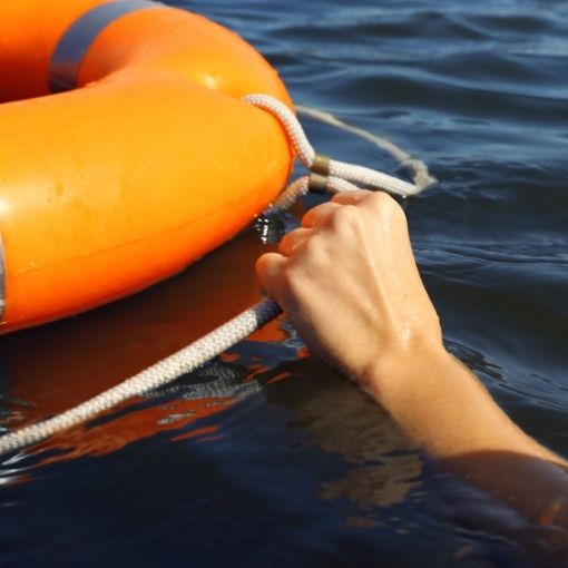 Hand gripping a rope attached to an orange lifebuoy floating on dark water.