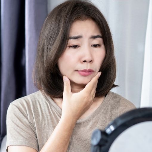 Woman looking worriedly at her reflection while touching her chin.