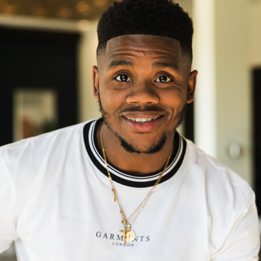 Young adult man wearing a white T-shirt and gold necklace standing indoors.