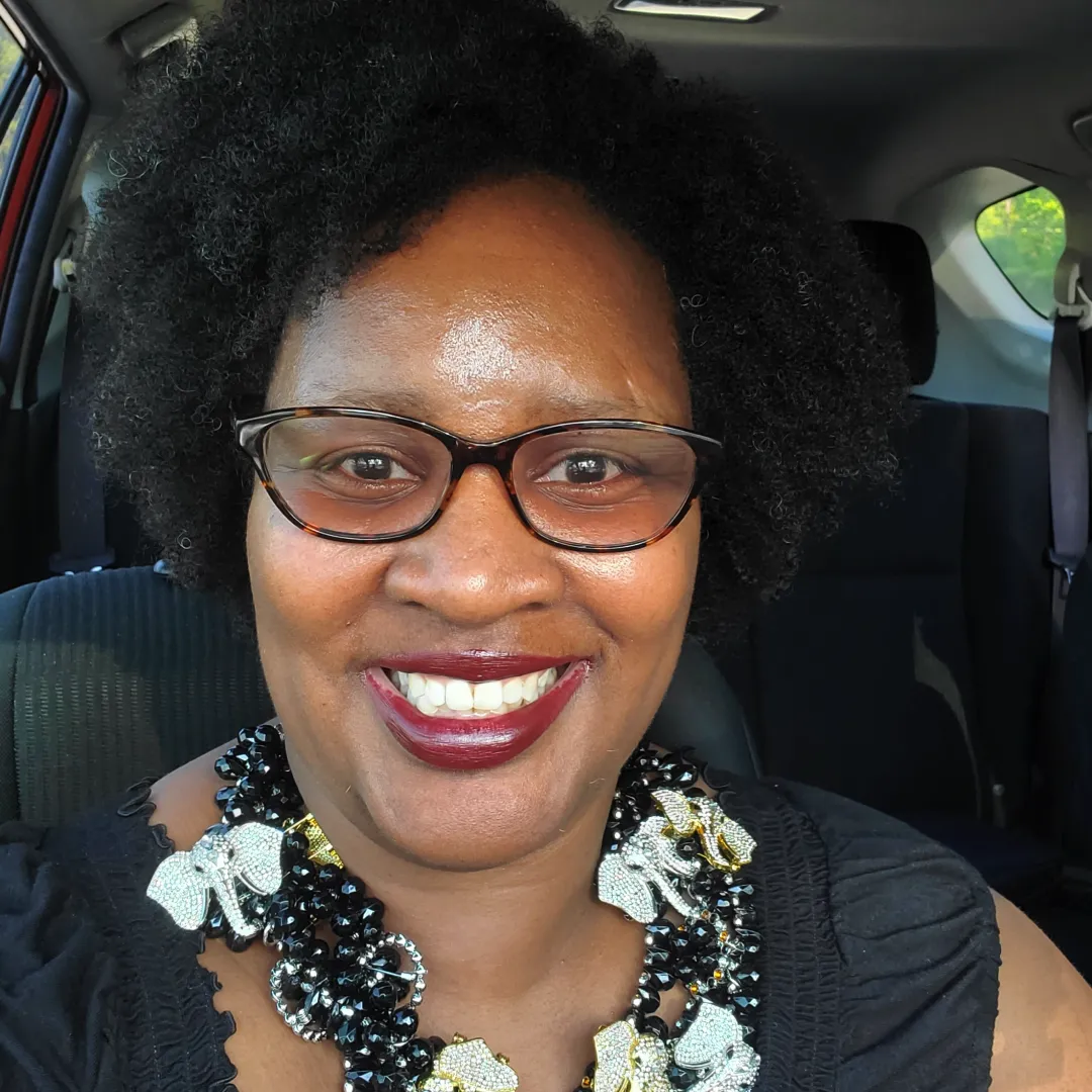 Woman with curly hair wearing a large beaded necklace smiling in a car.