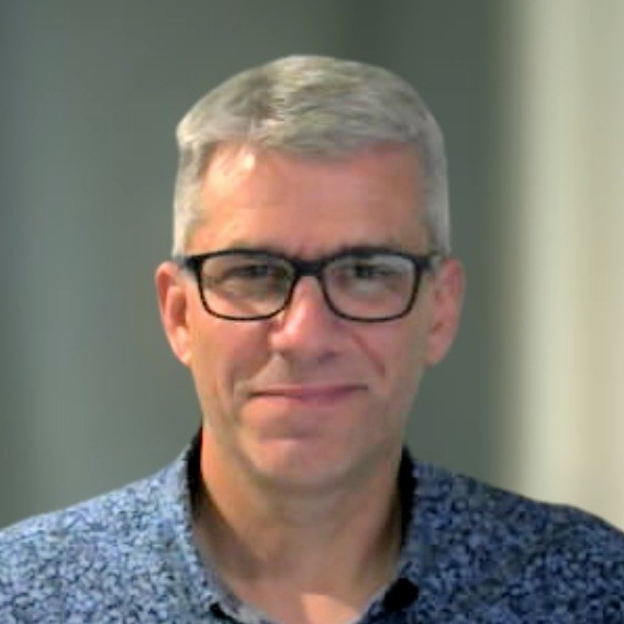 Middle-aged man with short gray hair wearing black glasses and a blue patterned shirt smiling slightly.