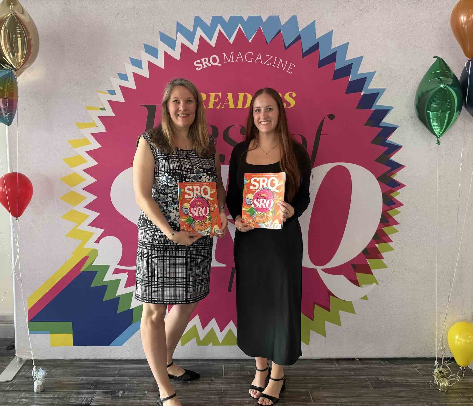 Audiologist smiling and holding a colorful SRQ magazine in front of a wall with a large 'Readers Best of SRQ local' graphic.